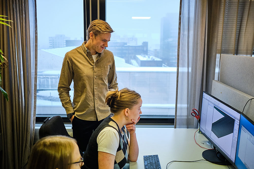 Kolme henkilöä työskentelee näytön ääressä