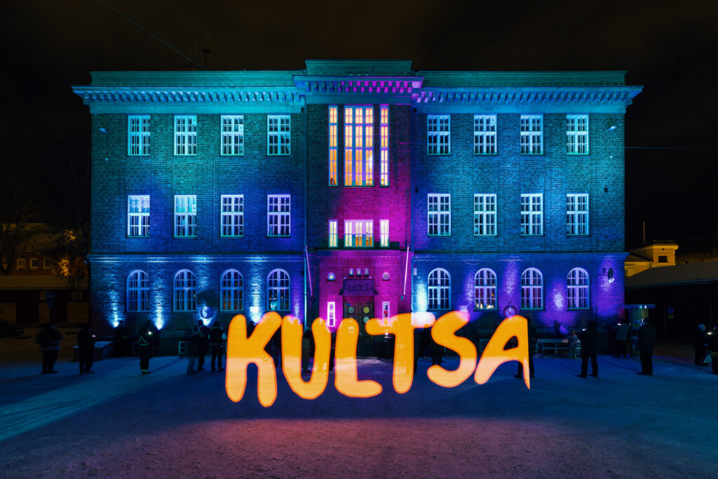 Sinisellä sävyllä valaistu rakennus, jonka edessä teksti "Kutsa"