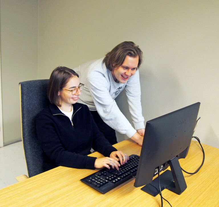 Kaksi henkilöä tietokoneen ääressä toimistossa.